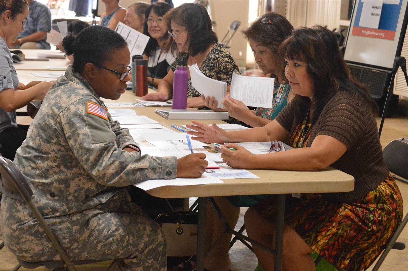 A soldier takes notes as volunteer mentors walk her through her resume at a veterans transition summit